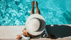 Femme assise au bord d'une piscine avec un chapeau