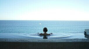 Femme de dos dans une piscine avec vue sur mer