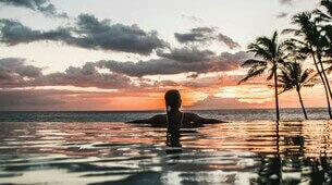 Femme de dos dans une piscine au coucher du soleil