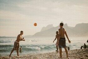 3 hommes jouent au foot sur la plage