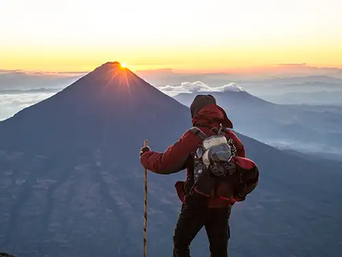 Homme équipé pour la randonnée devant un sommet au coucher du soleil