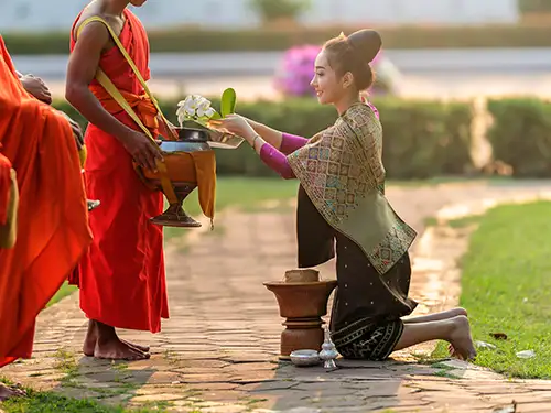 Femme à genoux qui offre des fleurs à un moine