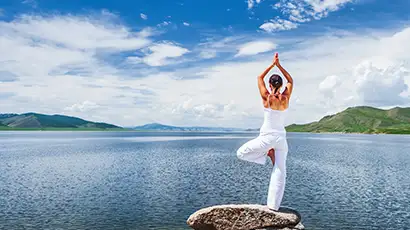 Femme de dos en posture de yoga devant un lac