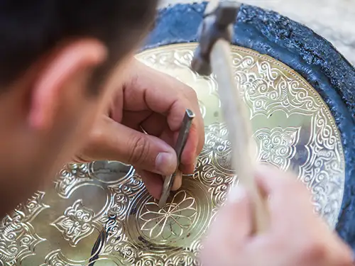 Homme qui sculpte de smotifs sur un plateau en argent